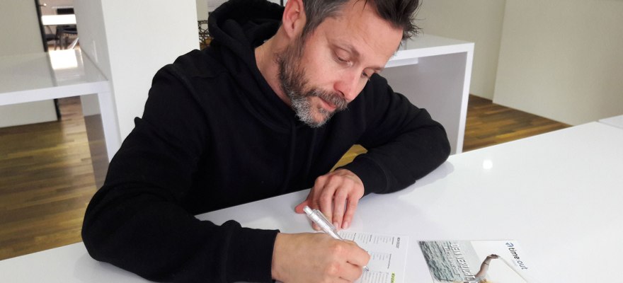 Radiomoderator Simon Mosers füllt auf einem weissen Tisch seine time:out-Anmeldung aus