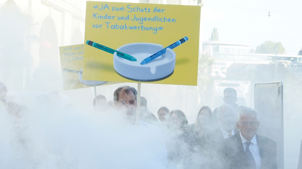 Politikerinnen und Politiker des Initiativkomitees gehen mit Transparenten durch eine Rauchwolke hindurch